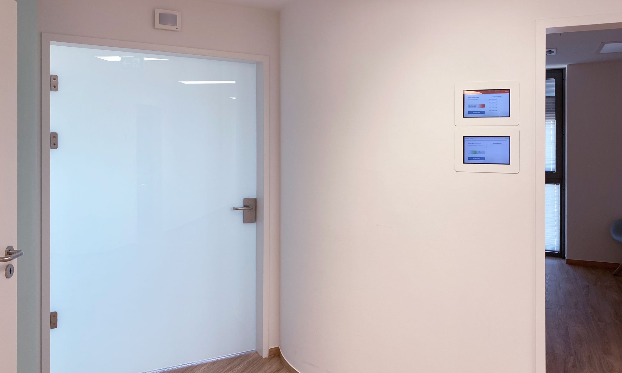 An einer Wand, bei einer Tür, hängen zwei Interaktive Türschilder