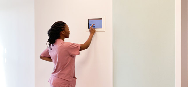 Eine Krankenschwester tippt auf ein Interaktive Türschild an der Wand