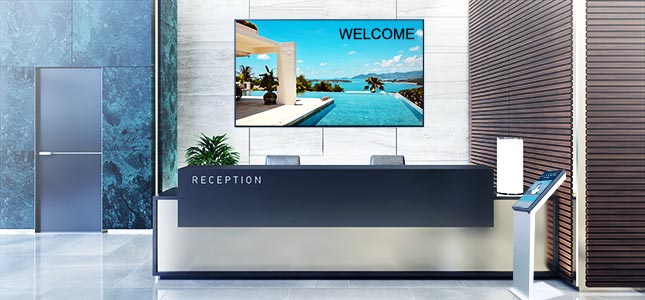 Eine Reception mit einem Display im Hintergrund und einem interaktiven Displaypult.